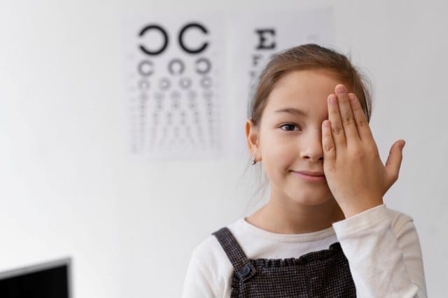 Niña en consulta con optometrista tapándose un ojo mientras realiza un examen de su visión