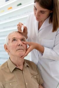 Persona mayor recibiendo gotas oftálmicas para glaucoma de una profesional