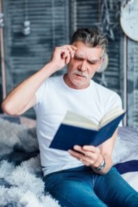 Hombre mayor con dificultad para leer cuando se quita las gafas de lectura