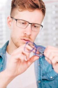 Hombre joven revisando meticulosamente sus gafas de lectura para saber si tienen un tratamiento especial