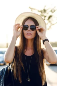Mujer joven con rostro cuadrado ajustándose sus gafas de sol mientras se prepara para un día de playa