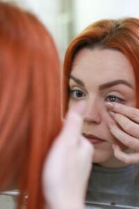 Mujer joven frente a un espejo colocándose su lente de contacto de última generación