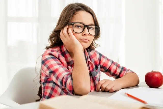Niño con hipermetropía utilizando sus gafas mientras realiza tareas escolares