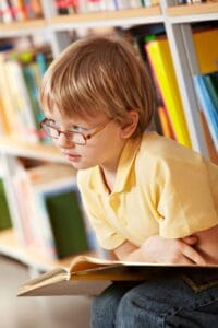 Niño con hipermetropía estudiando en la biblioteca de su colegio
